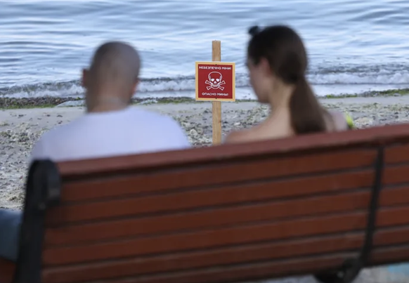 Un couple assis sur une plage d'Odessa. Face à lui: la mer et une tête de mort les prévenant de la présence de mines planquées sous le sable.