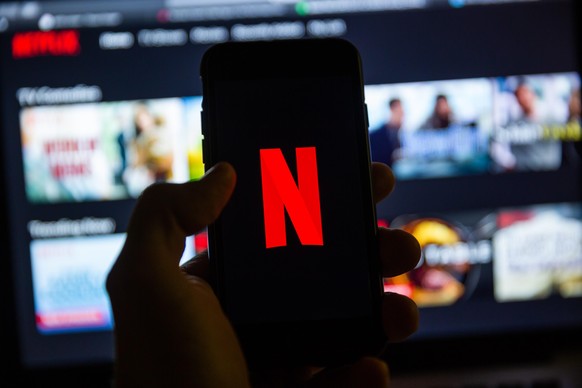 JANUARY 11, 2020: Man holds iPhone 7 with red Netflix brand logo on its screen in the evening. Netflix is a global video streaming service.