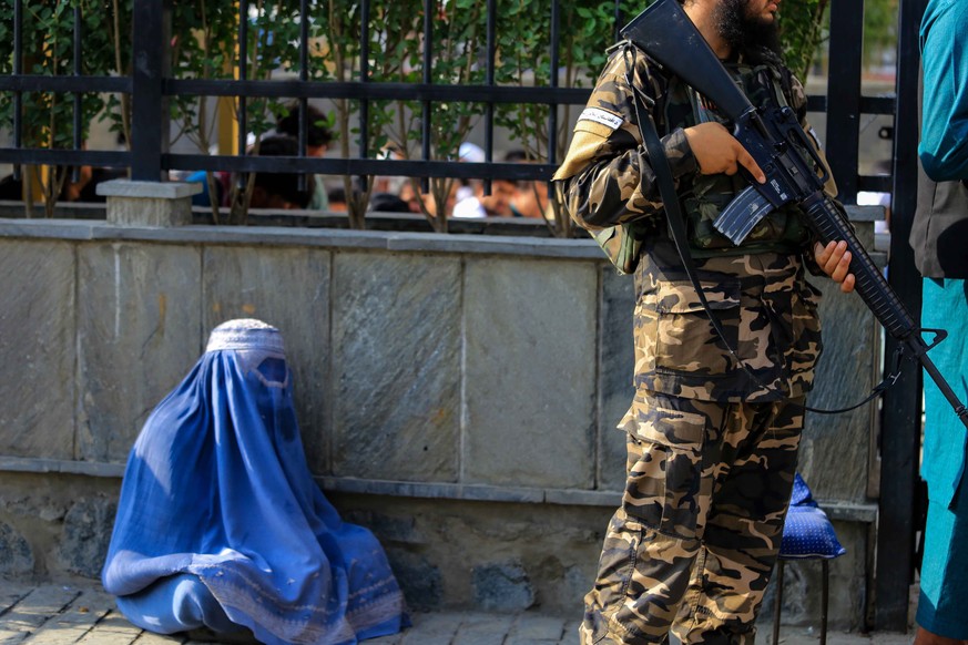 epa10093981 A burqa clad Afghan woman begs for alms as Taliban stand guard at a public place in in Kabul, Afghanistan, 27 July 2022. According to a report by non-governmental organization Amnesty Inte ...