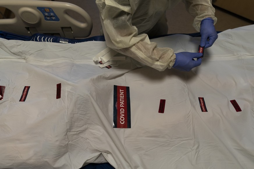 Registered nurse Bryan Hofilena attaches &quot;COVID Patient&quot; stickers on a body bag of a patient who died of coronavirus at Providence Holy Cross Medical Center in Los Angeles, Tuesday, Dec. 14, ...