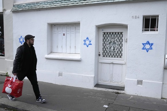 A man walks by Stars of David tagged on a wall Tuesday, Oct. 31, 2023 in Paris. Paris police chief Laurent Nunez described the graffiti as anti-Semitic and said police are investigating. (AP Photo/Mic ...