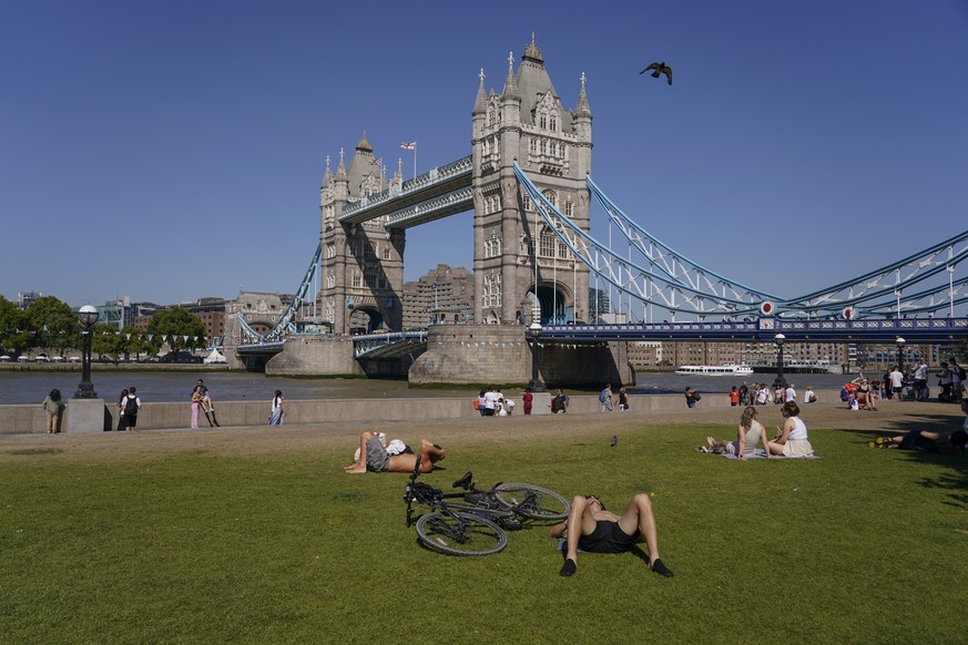 People sit and lay on the grass next to Tower Bridge, in London, Thursday, Aug. 11, 2022. Heatwaves and prolonged dry weather are damaging landscapes, gardens and wildlife, the National Trust has warn ...