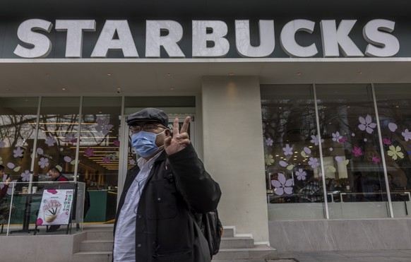 epa09064879 A man flashes the victory sign while passing by a Starbucks store in Shanghai, China, 10 March 2021. One year after the World Health Organisation (WHO) declared the pandemic of the COVID-1 ...