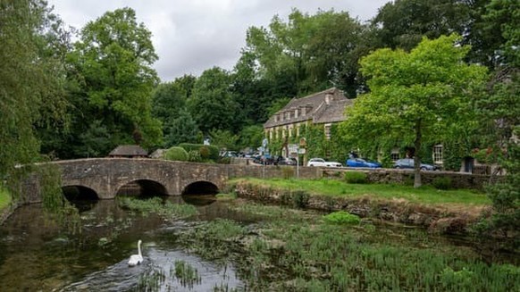 A Beautiful shot of stone cottage with a green garden and a river in Bibury Village