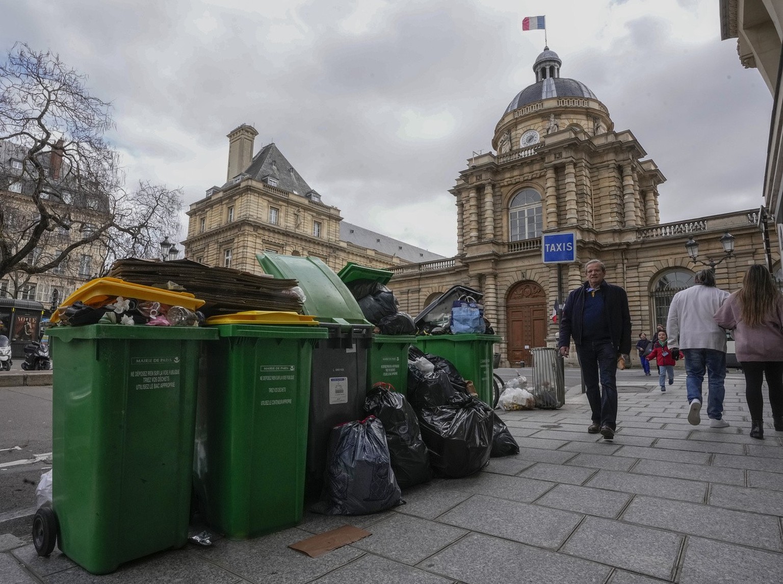 FILE- People walk past not collected garbage cans next to the Senate in Paris, Sunday, March 12, 2023. The City of Light is losing its luster with tons of garbage piling up on Paris sidewalks as sanit ...