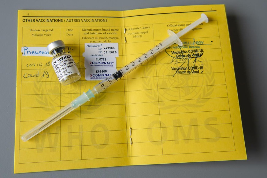 Une fiole du vaccin Pfizer-BioNTech et une seringue sont photographiees sur un carnet de l&#039;OMS de certificat international de vaccination ou de prophylaxie, faudra-t-il un jour un passeport vacci ...