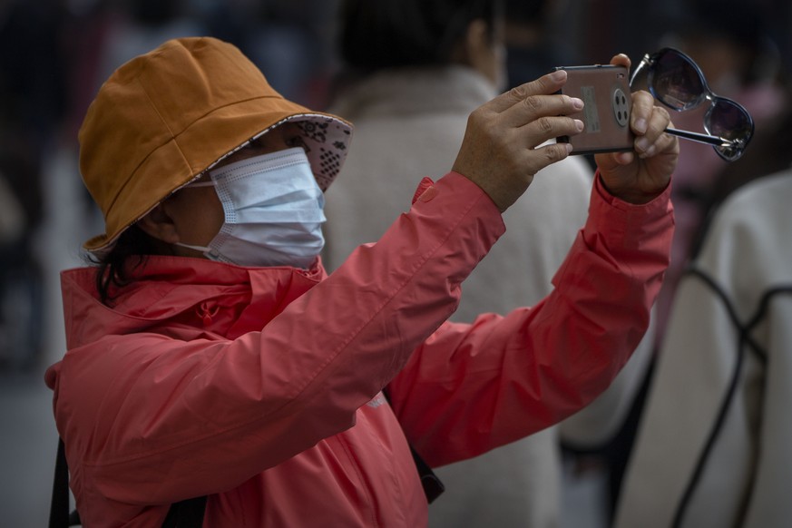 A woman wearing a face mask takes a smartphone photo along a tourist shopping street in Beijing, Friday, Oct. 7, 2022. Friday is the last day of China&#039;s National Day holiday period. (AP Photo/Mar ...