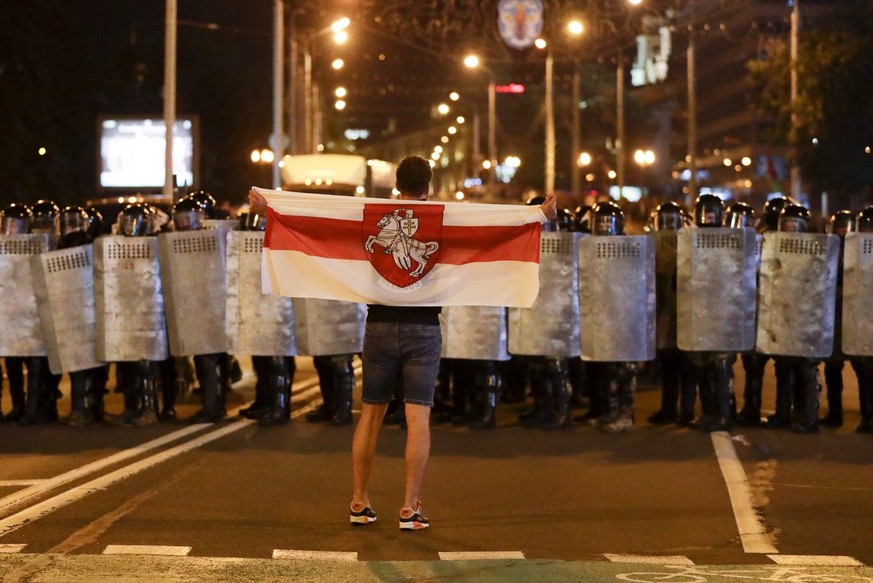 A protester holds an old Belarusian national flag as he stands in front of police line during a rally after the Belarusian presidential election in Minsk, Belarus, Sunday, Aug. 9, 2020. Police and pro ...