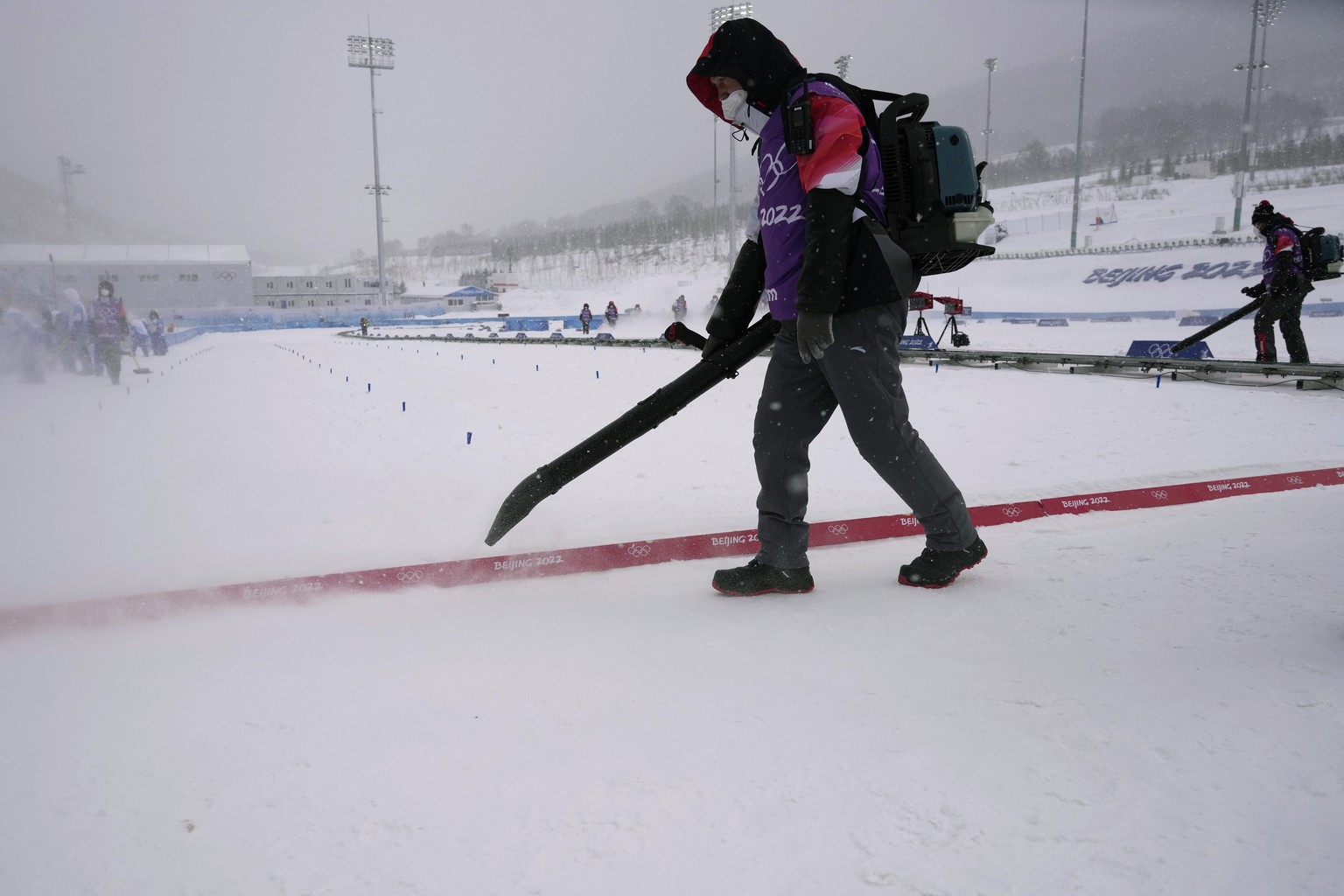 Workers clear the finish line of loose snow before the men's 4 x 10km relay cross-country skiing competition at the 2022 Winter Olympics, Sunday, Feb. 13, 2022, in Zhangjiakou, China. (AP Photo/A ...