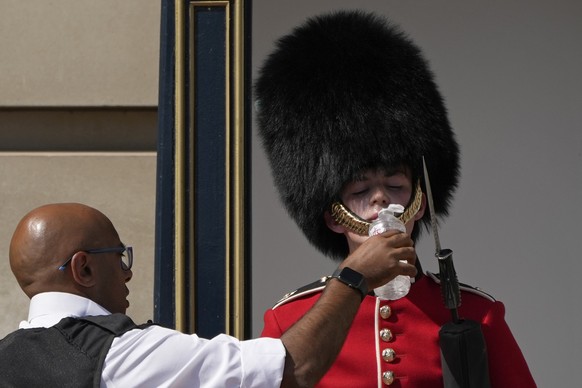 A police officer givers water to a British soldier wearing a traditional bearskin hat, on guard duty outside Buckingham Palace, during hot weather in London, Monday, July 18, 2022. The British governm ...