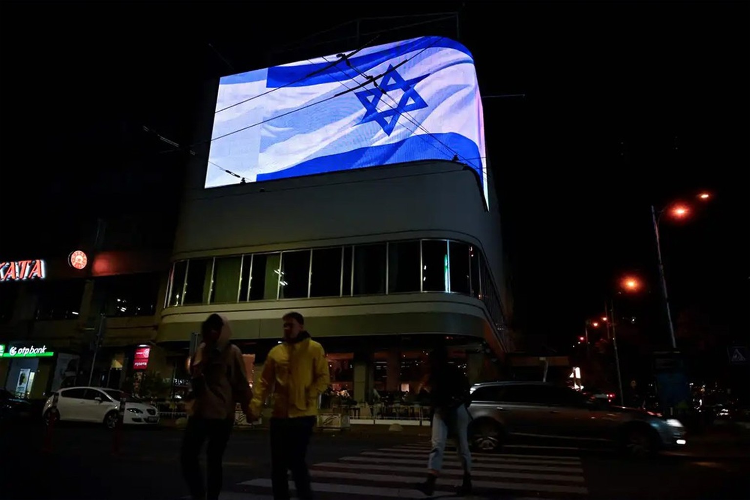 Des piétons traversent une rue devant un drapeau national israélien affiché sur un écran géant dans la capitale ukrainienne, Kiev, le 8 octobre 2023.