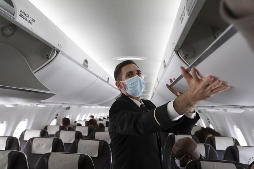 A cabin crew member of Swiss International Air Lines wearing a face mask to protect against the spread of coronavirus COVID-19 prepares the aircraft prior to departure to London during the resumption  ...