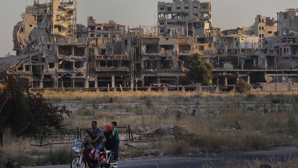 FILE - People ride their motorcycle by damaged buildings in the old town of Homs, Syria, Aug. 15, 2018. Syria?s civil war has entered its 14th year on Friday March 15, 2024, a somber anniversary in a  ...