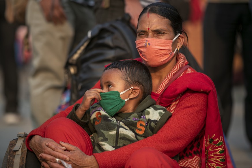 A Nepalese woman with her child waits for a bus to go back to her village a day prior to lockdown in Kathmandu, Nepal, Wednesday, April 28, 2021. Tens of thousands of people left the Nepalese capital  ...
