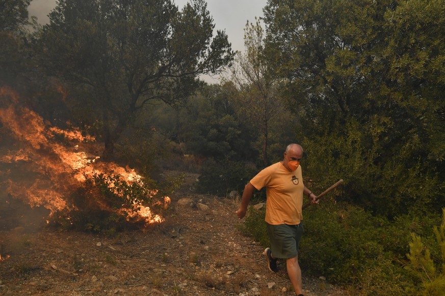 A man passes next to flames during a fire in northern Athens, Monday, Aug. 12, 2024, as hundreds of firefighters tackle a major wildfire raging out of control on fringes of Greek capital. (AP Photo/Mi ...