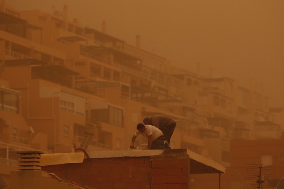 epa09825988 Two men work on the roof of a building as dust from the Sahara desert blankets the coastal city of Roquetas de Mar, Spain, 15 March 2022. A wave of airborne dust from the Sahara is moving  ...