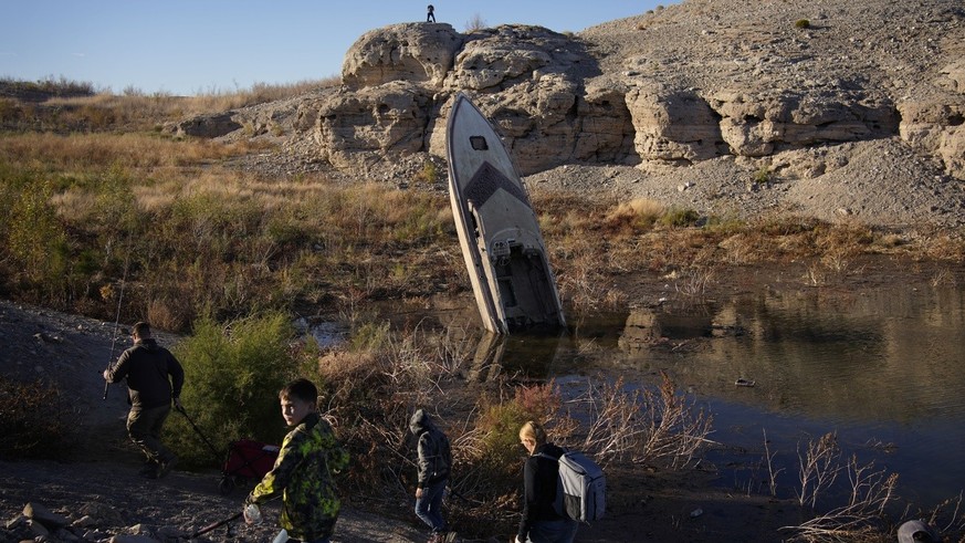 FILE - People walk by a formerly sunken boat standing upright into the air with its stern buried in the mud along the shoreline of Lake Mead at the Lake Mead National Recreation Area, Friday, Jan. 27, ...