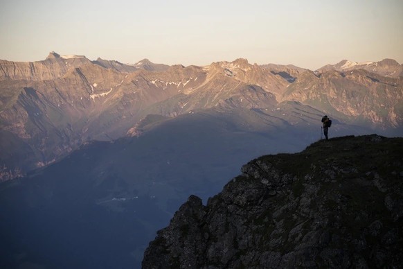 Paysage de montagne en été, au petit matin, avec une silhouette de randonneur au sommet d'un massif rocheux.