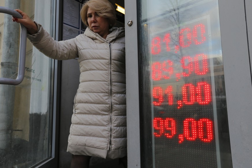 In this Feb. 24, 2022, photo, a woman leaves an exchange office with screen showing the currency exchange rates of U.S. Dollar and Euro to Russian Rubles in Moscow, Russia. The harsh sanctions imposed ...