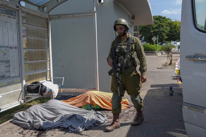 An Israeli soldier stands by the bodies of Israelis killed by Palestinian armed militants who entered from the Gaza strip, in the southern Israeli city of Sderot, Saturday, Oct. 7, 2023. Hamas, the mi ...