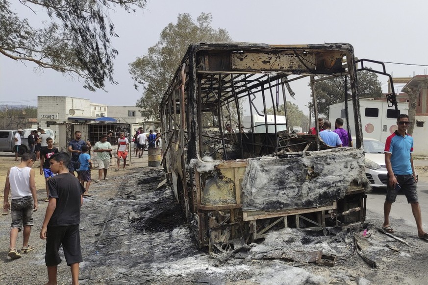 Residents walk past a charred truck in El Kala, in the El Tarf region, near the northern Algerian-Tunisian border, Thursday, Aug.18, 2022. Wildfires raging in the forests of eastern Algeria have kille ...