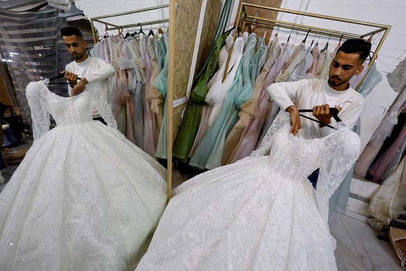 A Palestinian man holds a wedding dress at a shop with damaged walls, as brides in Gaza turn to reused gowns amid soaring prices and shortages caused by the war, in Khan Younis in the southern Gaza St ...