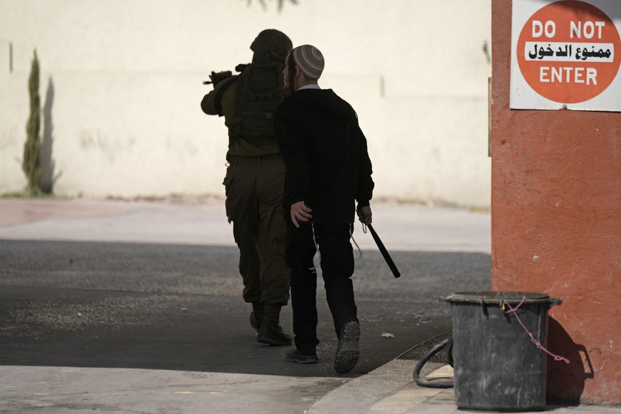 An Israeli settler with a weapon stands behind an Israeli soldier during clashes after Israeli settlers attacked Palestinians in Huwara, near the West Bank town of Nablus, Thursday, Oct. 13, 2022. (AP ...