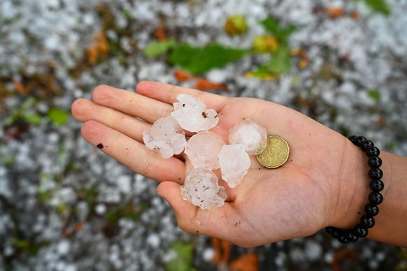 20.08.2026, Bayern, Monheim: Gro�e Hagelk�rner liegen nach einem Unwetter auf einer Hand neben einem 20-Cent-St�ck. Die Landschaft war stellenweise von einer dicken Schicht aus Hagelk�rnern bedeckt. F ...