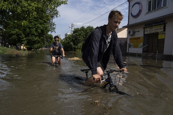 Local residents try to ride their bikes along a flooded road after the Kakhovka dam blew overnight, in Kherson, Ukraine, Tuesday, Jun 6, 2023. Ukraine on Tuesday accused Russian forces of blowing up a ...