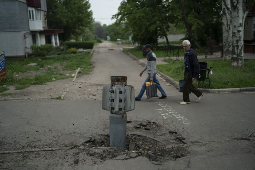 People walk past part of a rocket that sits wedged in the ground in Lysychansk, Luhansk region, Ukraine, Friday, May 13, 2022. (AP Photo/Leo Correa)