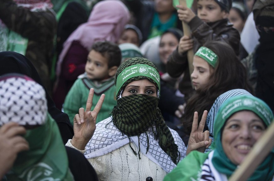 A Palestinian woman flashes the victory sign and wears a headband with Arabic that reads: "No God but Allah and Muhammed is his messenger, al-Qassam Brigades" during a mass rally marking the ...