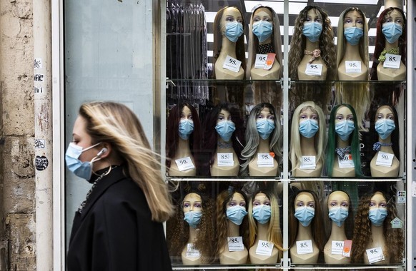 epa08780314 A woman wearing a protective face mask walks past a shop window displaying mannequin heads with masks, in Paris, France, 28 October 2020. France is in the midst of a second wave of the COV ...
