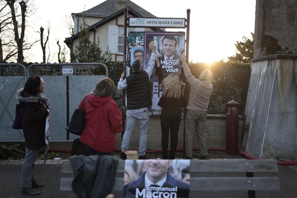 Emilien Varenne, center, Marie-Laure Rouffy-Morice , second right, and Jean-Pierre Bedouin stick electoral poster of French President Emmanuel Macron and centrist candidate for reelection, Tuesday, Ma ...