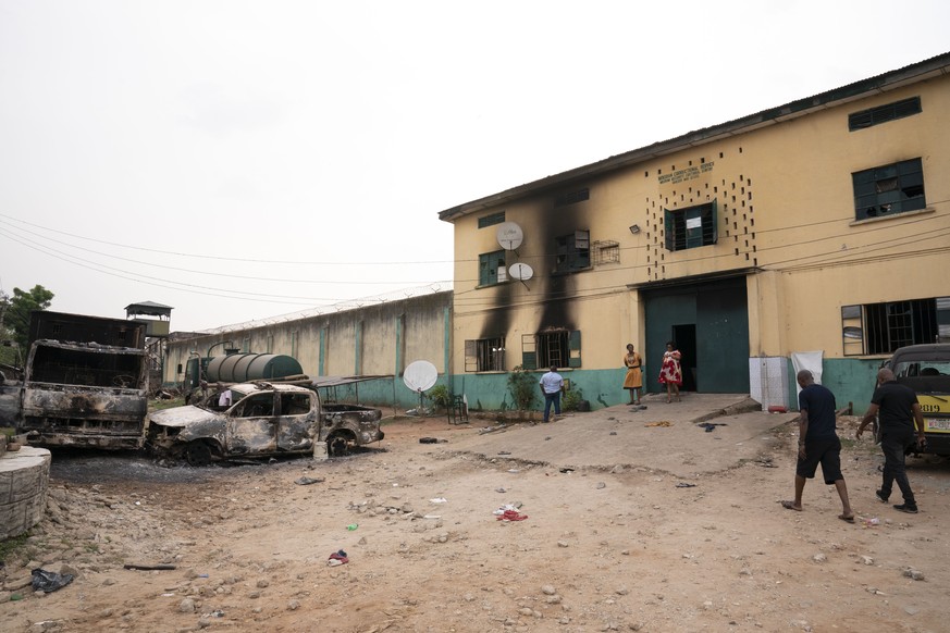 People walk past burned vehicles in front of a correctional facility in Owerri, Nigeria, on Monday, April 5, 2021. Hundreds of inmates escaped from the prison in southeastern Nigeria after a series of ...