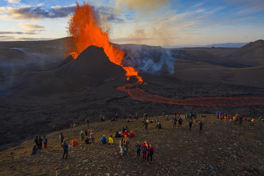 People watch as lava flows from an eruption from the Fagradalsfjall volcano on the Reykjanes Peninsula in southwestern Iceland on Tuesday, May 11, 2021. The glow from the bubbling hot lava spewing out ...