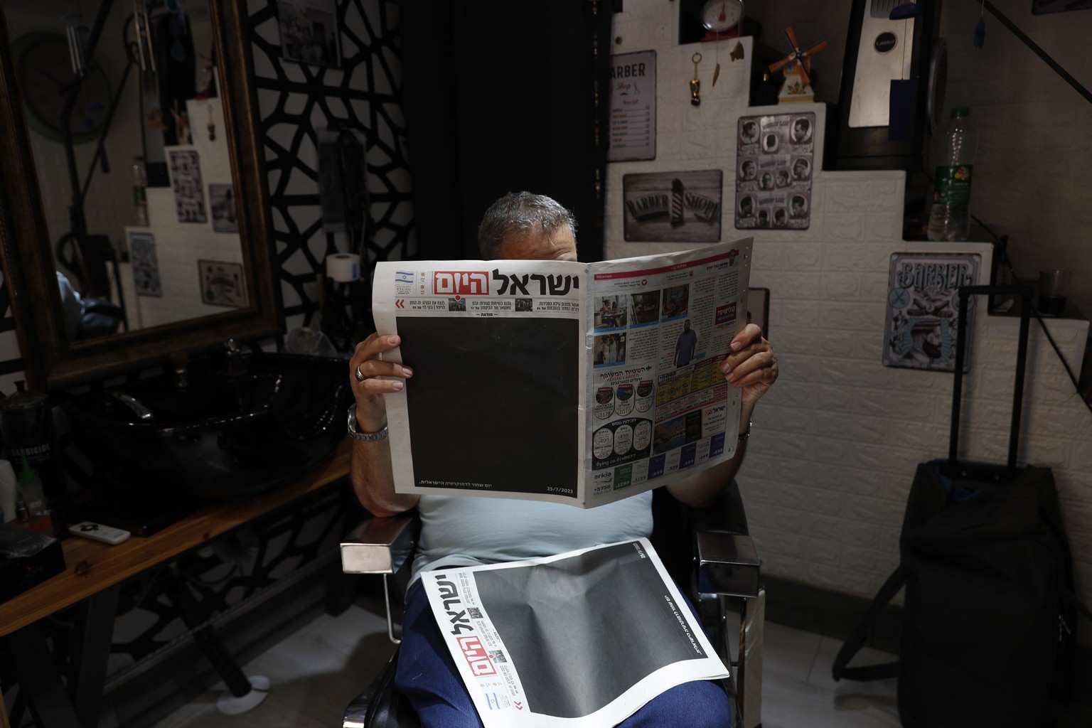 epa10767614 An Israeli hairdresser holds a copy of &#039;Israel Hayom&#039; (Israel Today) newspaper with blacked out front page and headline reading in Hebrew &#039;Black Day for Israeli Democracy&#0 ...