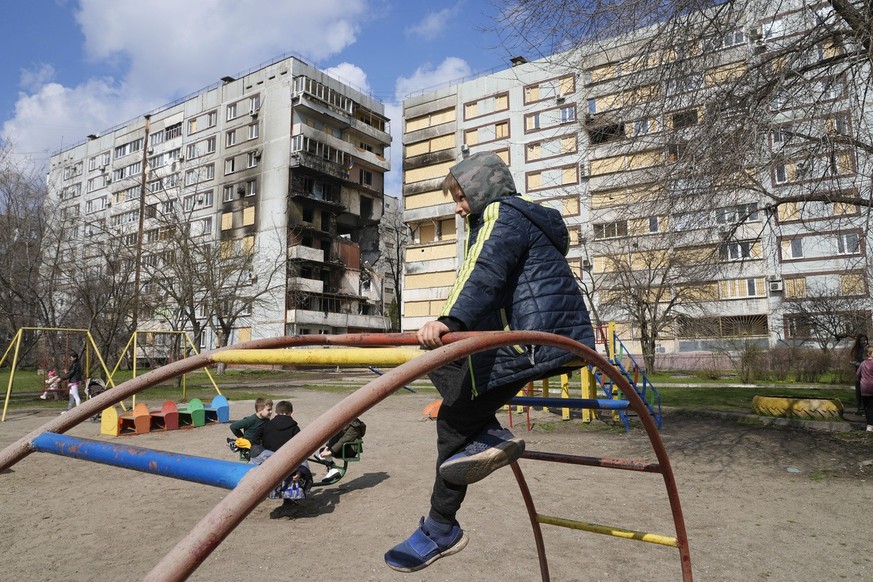 Children play in a playground in front of missile-damaged buildings ahead of a visit by Ukraine&#039;s President Volodymyr Zelenskyy Zaporizhzhia, Ukraine, Monday March 27, 2023. (AP Photo/Efrem Lukat ...