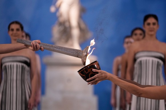 High Priestess Mary Mina, left, lights a torch from the Olympic flame during the flame lighting ceremony for the Milan Cortina 2026 Winter Olympics, at the archaeological museum of Olympia, Greece, We ...