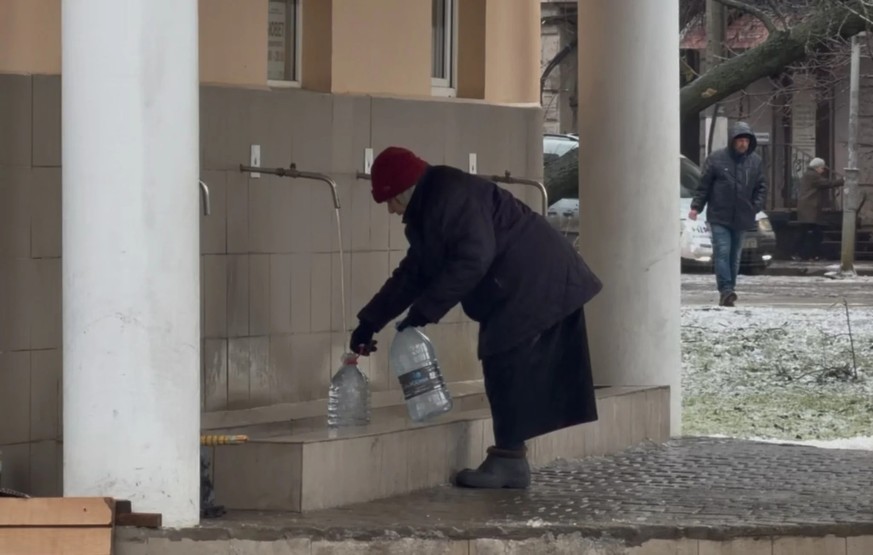 Une vieille femme remplit des bouteilles d'eau à une fontaine publique.