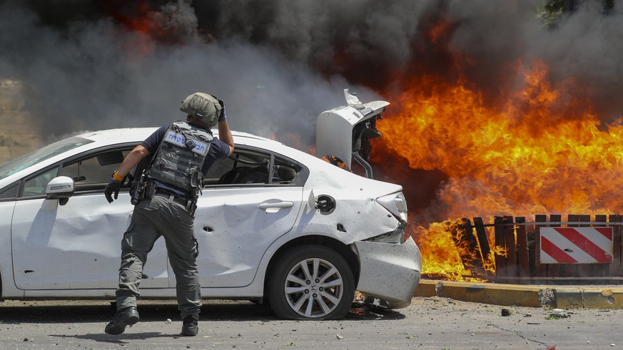 A member of Israeli bomb squad looks at burning cars that were set on fire by a missile fired from the Gaza Strip, in the southern Israeli town of Ashkelon, Tuesday, May 11, 2021. (AP Photo/Ariel Scha ...