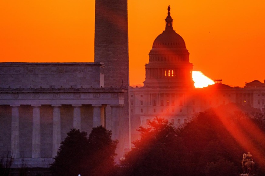 The sun flares through the camera lens as it rises behind the U.S. Capitol building, Washington Monument and the Lincoln Memorial, Monday, March 22, 2021, in Washington. (AP Photo/J. David Ake)