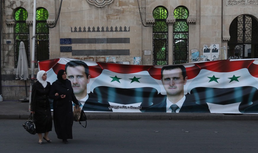 epa09209678 People walk next to a campaign banner of Syria President Bashar Assad as a candidate for the presidential elections, in Damascus, Syria, 18 May 2021. Three candidates, including the curren ...