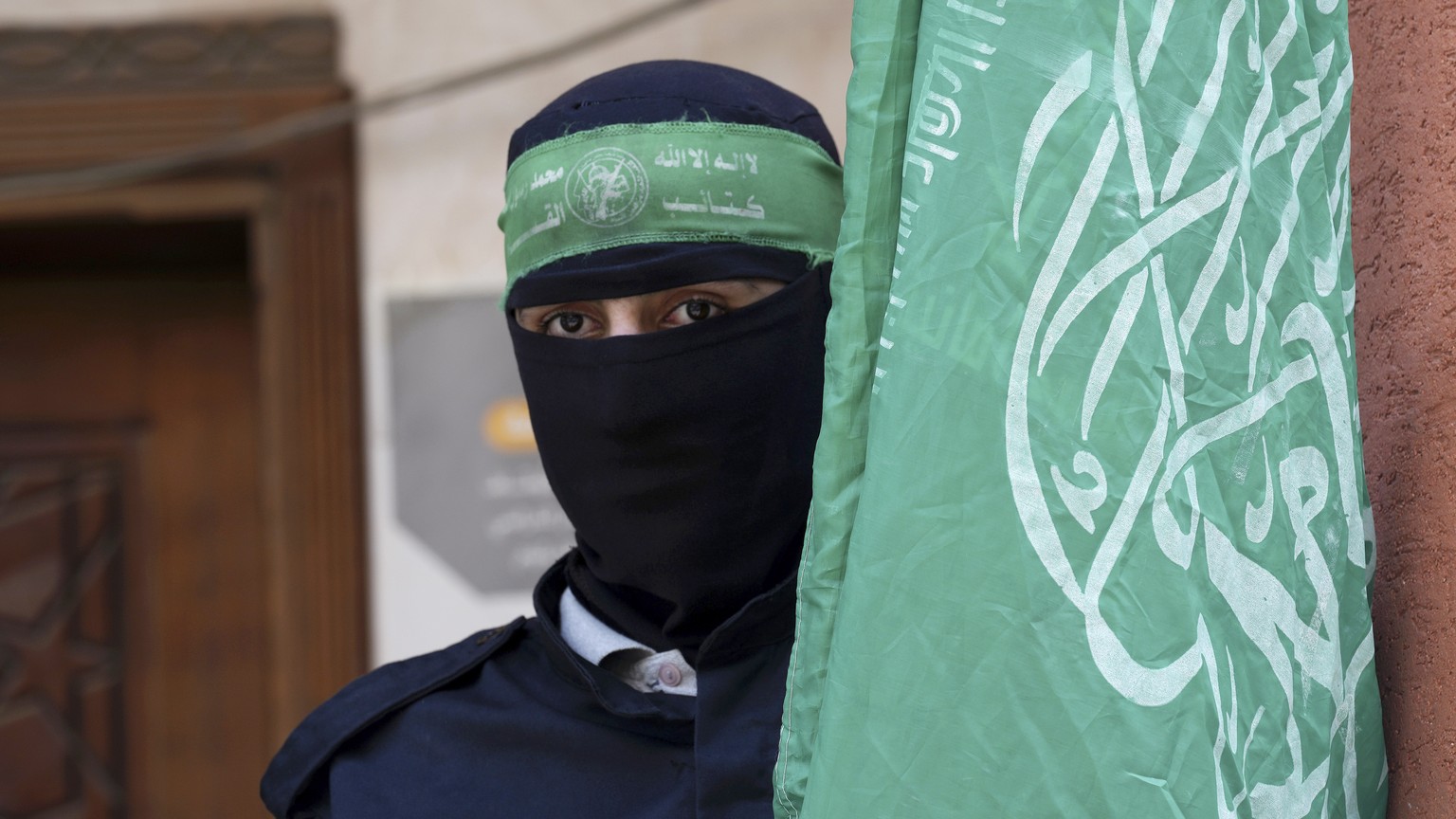 Masked militant from the Izzedine al-Qassam Brigades, the military wing of Hamas, waves the green flag of the Islamist group during a protest in support of Palestinian prisoners in Israeli jails, afte ...