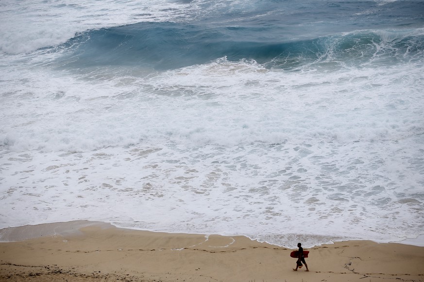 FILE - A boogie boarder walks near the surf at Makapu&#039;u Beach, Friday, Aug. 24, 2018, in Waimanalo, Hawaii, as Hurricane Lane approaches Oahu and large ocean swells impact the coastline. In a rep ...