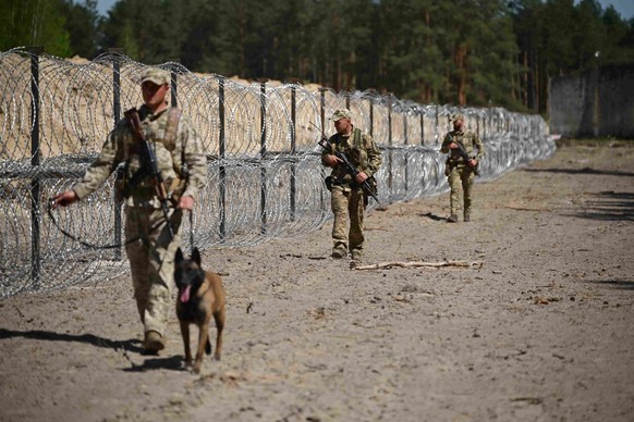 Des gardes-frontières ukrainiens patrouillent un tronçon de la frontière entre l'Ukraine et la Biélorussie, le long d'une clôture grillagée et barbelée.