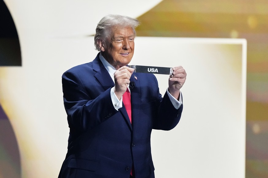 President Donald Trump holds his country&#039;s card during the draw for the 2026 soccer World Cup at the Kennedy Center in Washington, Friday, Dec. 5, 2025. (AP Photo/Stephanie Scarbrough, Pool)