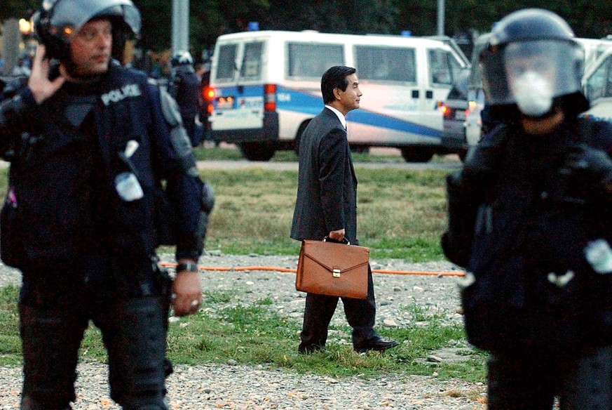 Un homme d'affaire semble perdu au milleu de policiers anti-emeute, ce mardi 3 juin 2003 sur la place de Plainpalais a Geneve, durant une manifestation anti-G8. (KEYSTONE/Martial Trezzini)