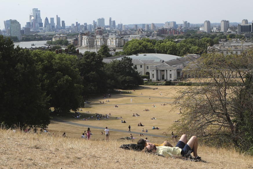 People sit on the sun-parched grass in Greenwich Park with the City of London skyline in the background in London, Sunday July 17, 2022. Britain&#039;s weather agency has issued its first-ever &quot;r ...