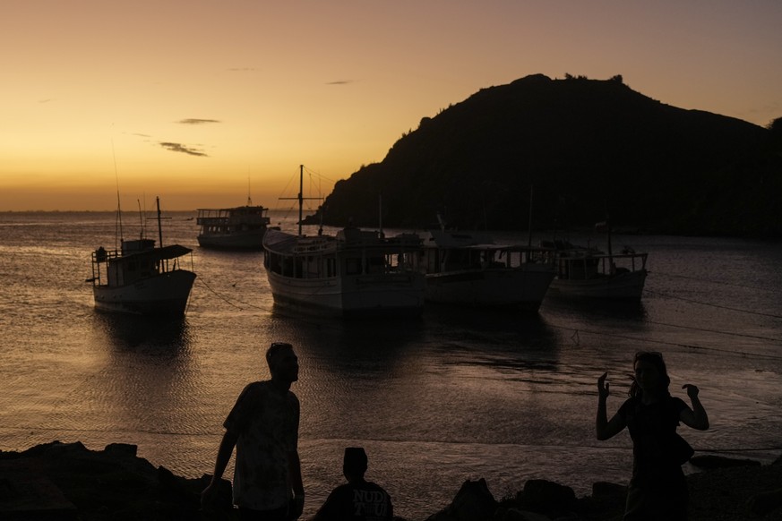People stand on the shore as the sun sets on Margarita Island, Venezuela, Friday, Jan. 12, 2024. (AP Photo/Matias Delacroix)