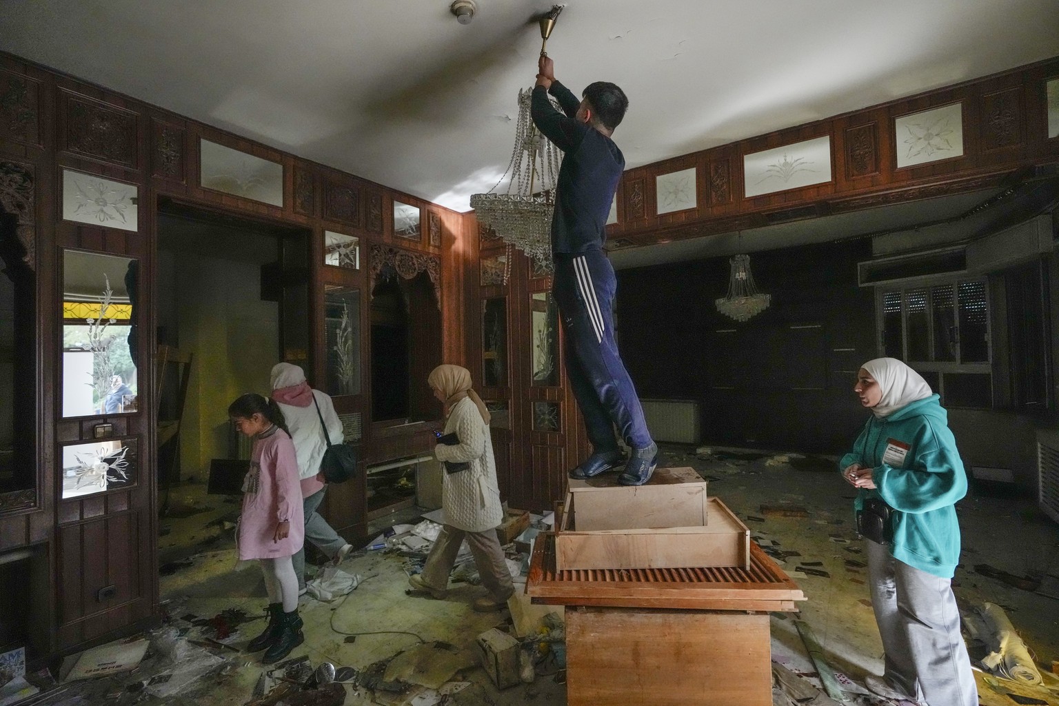 A man tries to take a chandelier as people search for belongings in the ransacked private residence of Syrian President Bashar Assad in the Malkeh district of Damascus, Syria, on Sunday, Dec. 8, 2024. ...